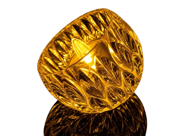 Elevate your home ambiance with this exquisite amber-tinted crystal glass tea light holder. Featuring a unique scalloped, diamond-faceted pattern, it beautifully scatters and diffuses light to create an enchanting atmosphere. Styled on a sleek reflective surface, it highlights a warm LED flame bulb that provides a safe, cozy, and luxurious sparkle. Ideal for mantle decorations, wedding centerpieces, festive gatherings, or everyday serene lighting. Warm Amber Faceted Crystal Glass Tea Light Holder