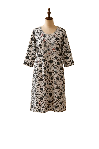 A straight-cut midi cotton kurti displayed on a dress mannequin. The garment features a dense, all-over botanical and floral print in jet black on an ivory cream background. The scoop neckline and upper bodice are detailed with delicate white and soft orange thread embroidery. The three-quarter sleeves are straight with a matching continuous floral print.